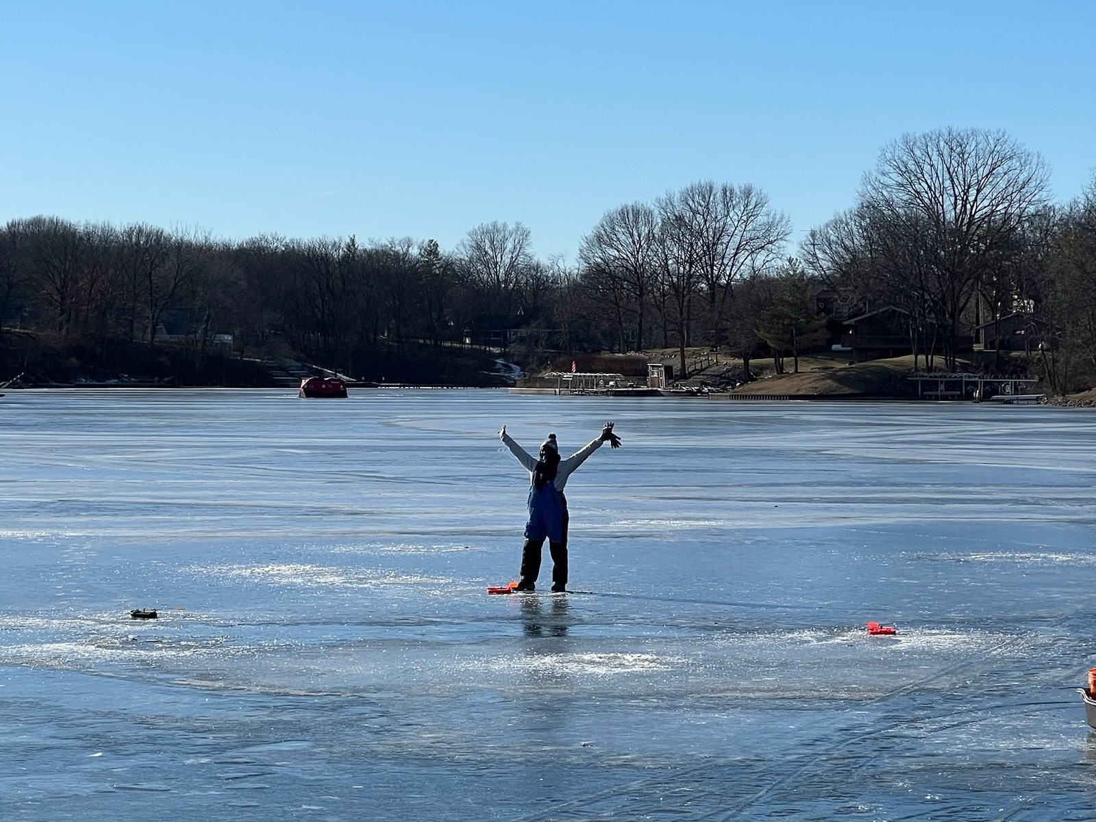 A person in winter gear stands on a frozen lake, arms raised in joy.